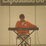 Arden playing a keyboard with Exposalud sign in background